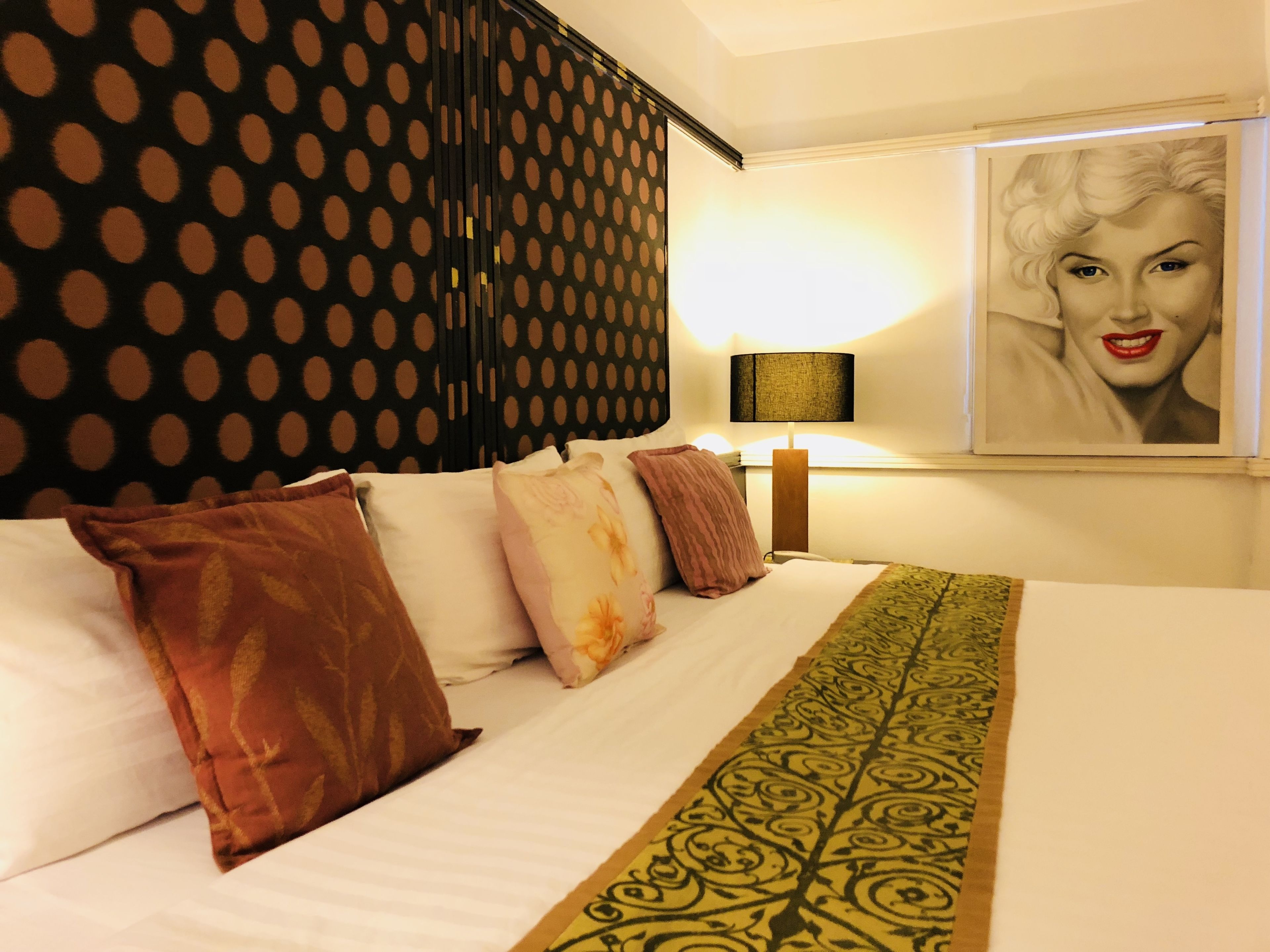 A hotel room with a bed, pillows, a lamp, and a framed picture on the wall.