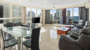 Amplia sala de estar con mesa de vidrio, sofá de cuero y balcón con vistas a la ciudad.