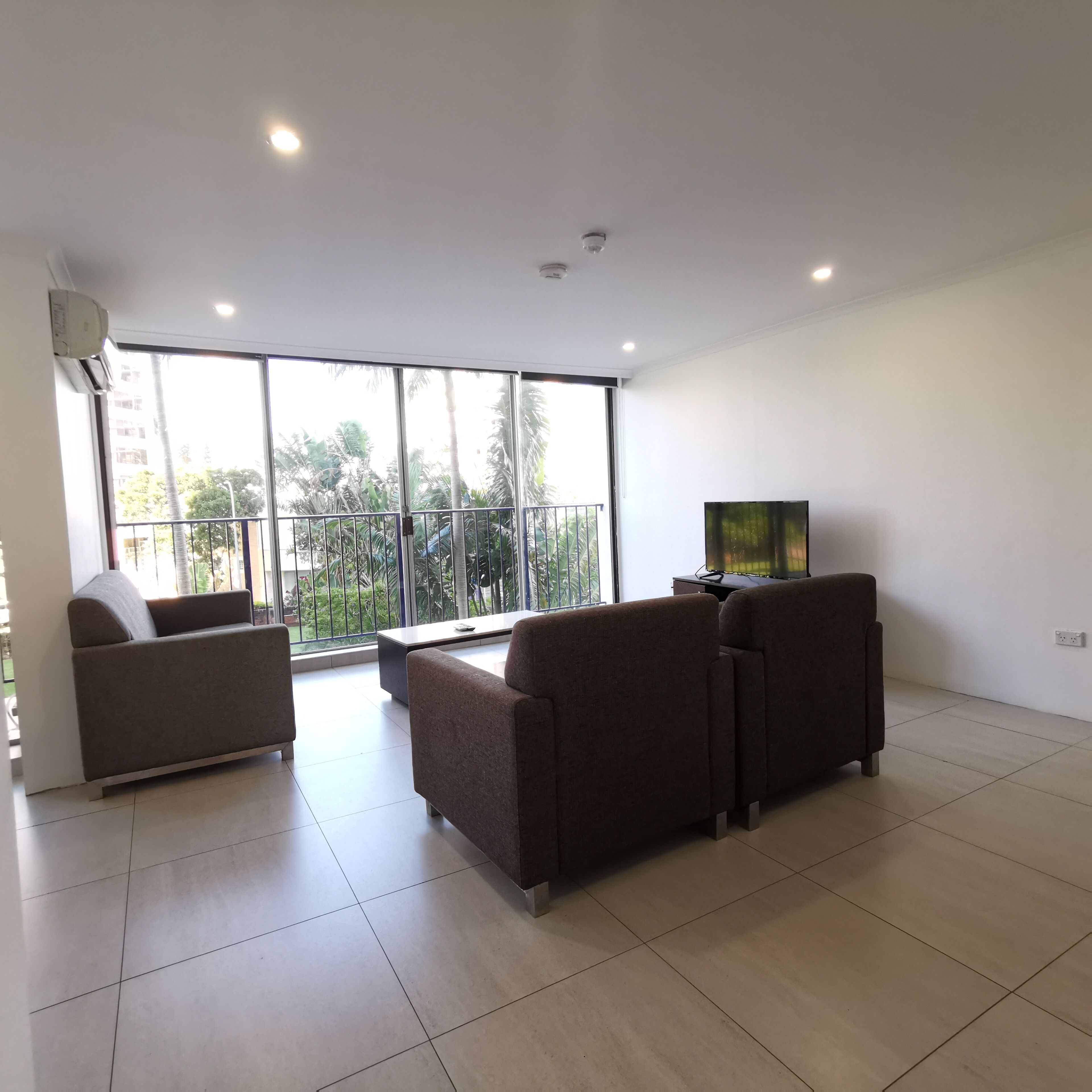 A spacious living room with a large window, a flat-screen TV, and a sofa.