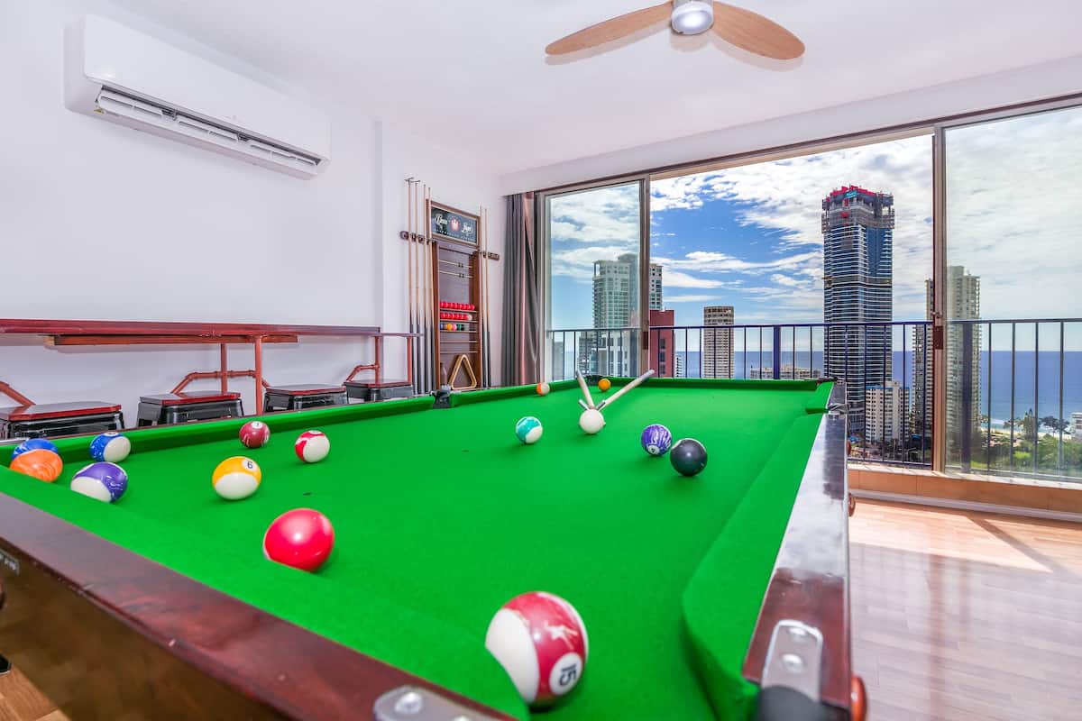A pool table with balls, a ceiling fan, and a view of a cityscape through large windows.