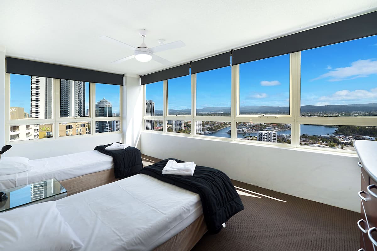 A hotel room with two beds, a ceiling fan, and a large window offering a city view.