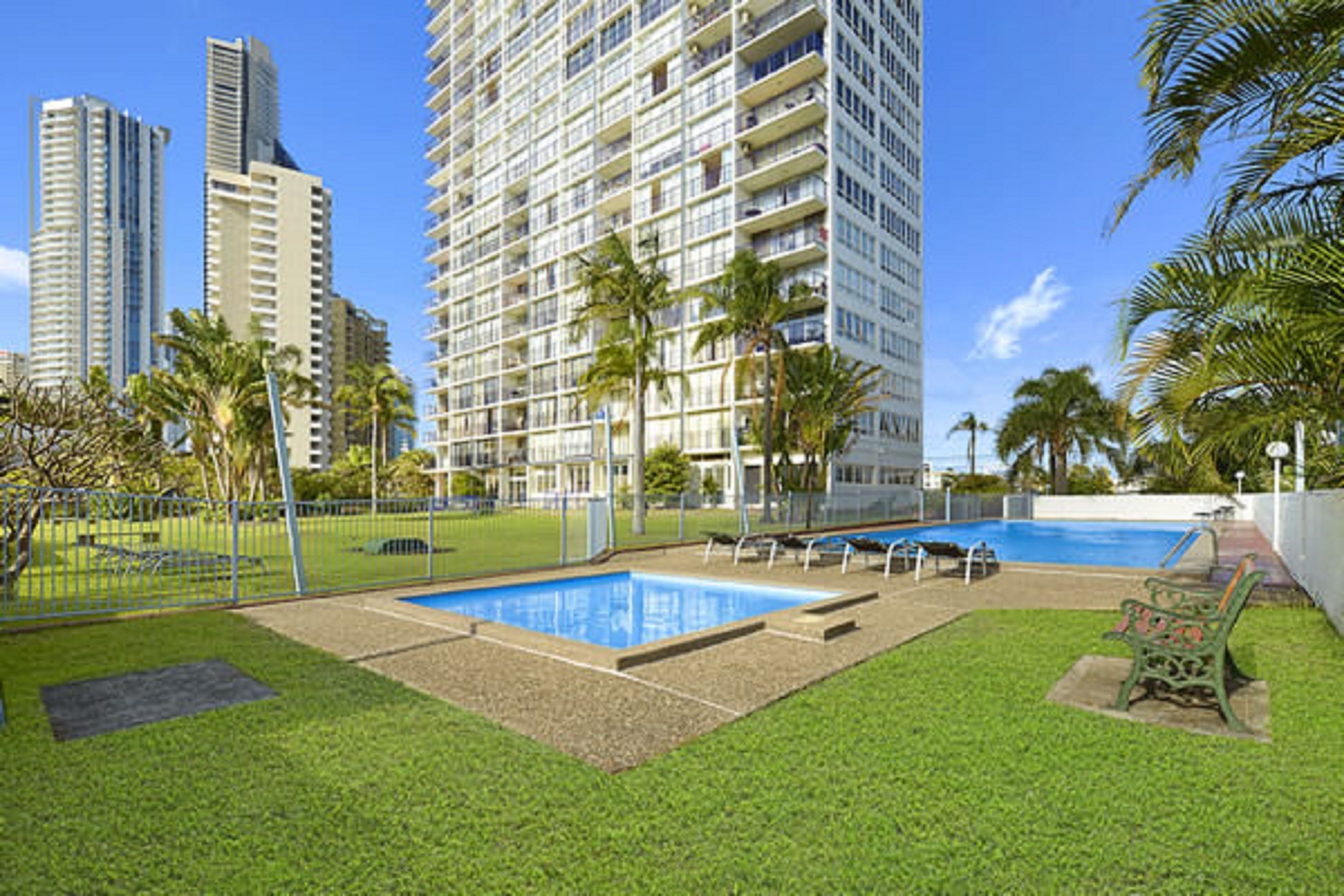 A high-rise building with a swimming pool and palm trees.