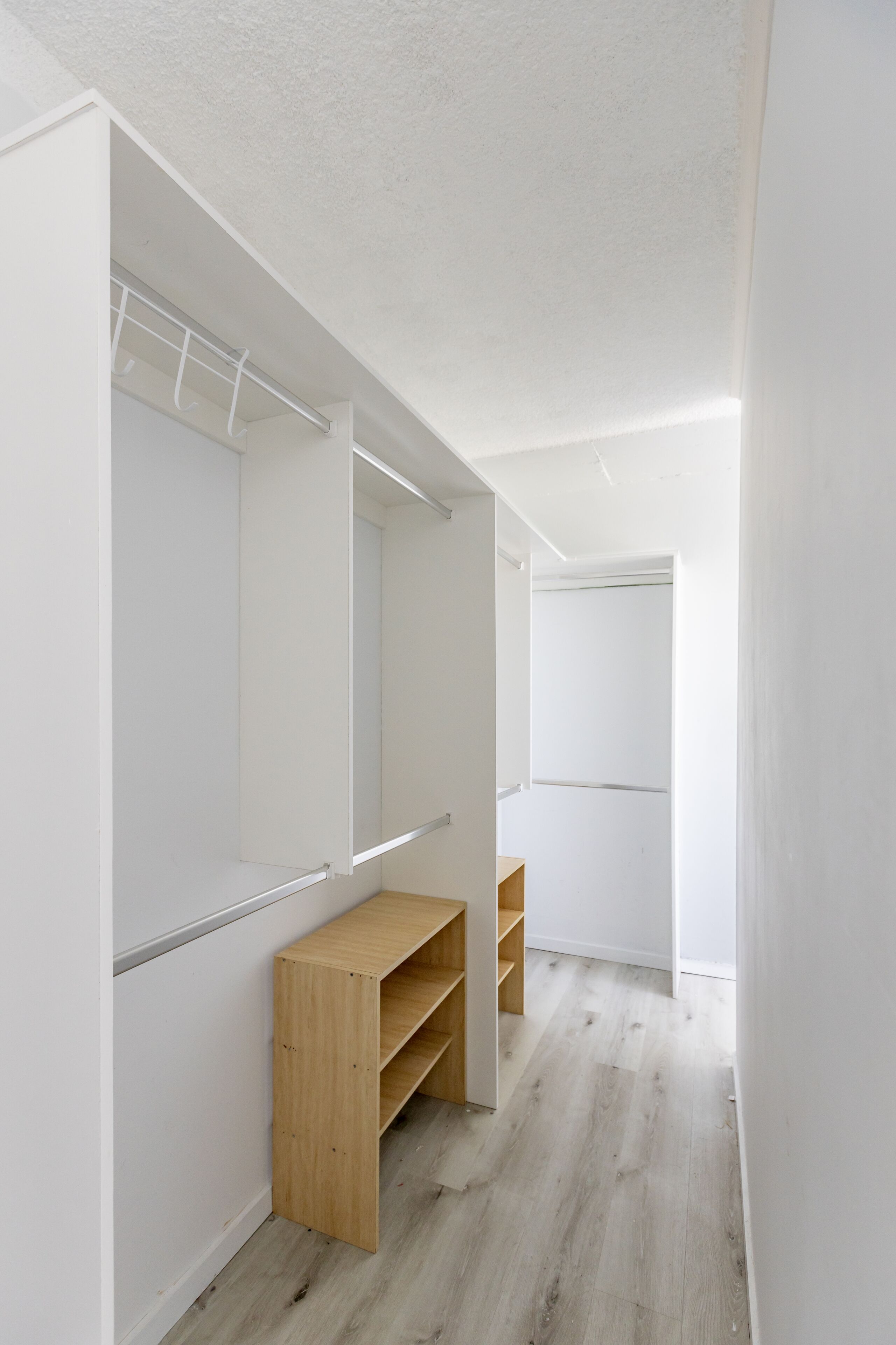 Un couloir étroit aux murs blancs, avec un banc en bois et une porte de placard à miroir.