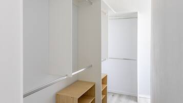 Un couloir étroit aux murs blancs, avec un banc en bois et une porte de placard à miroir.