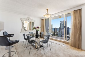Un comedor moderno con una mesa y sillas de vidrio, un espejo decorativo y vistas de la ciudad a través de amplias ventanas.