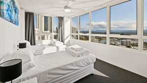 Habitación de hotel con cama, escritorio, silla, lámpara y ventanas amplias que dan a una vista de la ciudad.