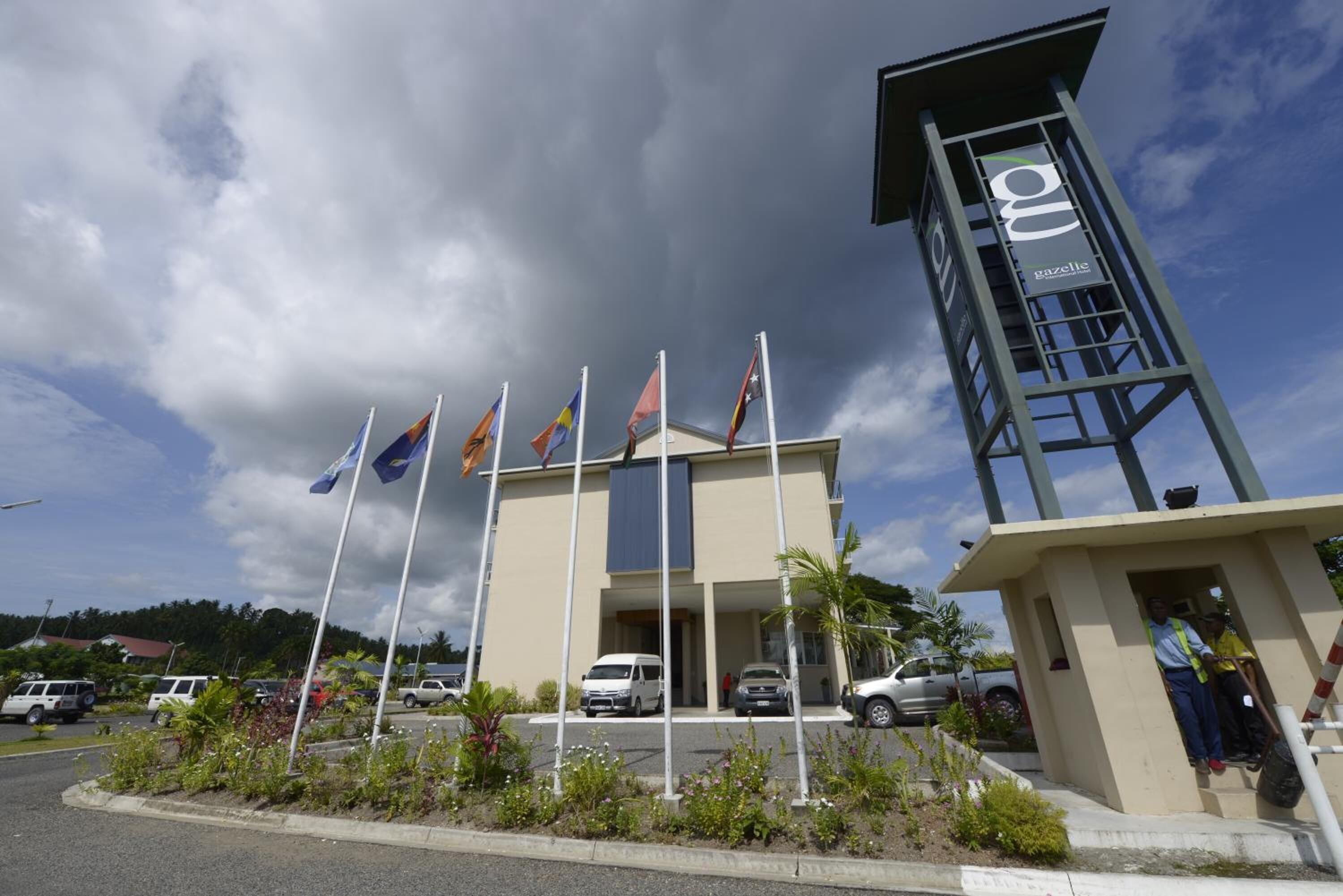 A building with multiple flags, a tower with a sign, and a parking lot.