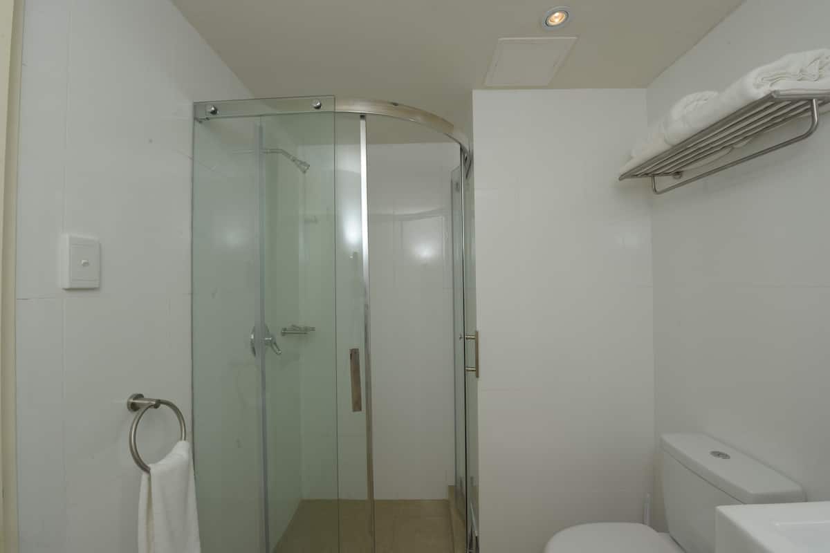 Een douchecabine met glazen wanden, een handdoekrek en een toilet in een witte badkamer.