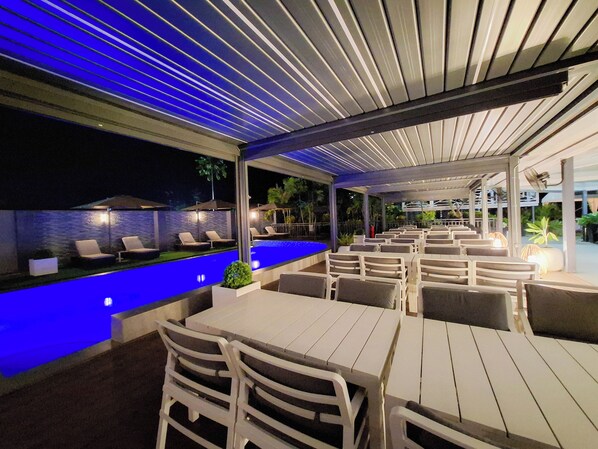 Un área de comedor al aire libre con piscina, sillones de descanso y mesas.