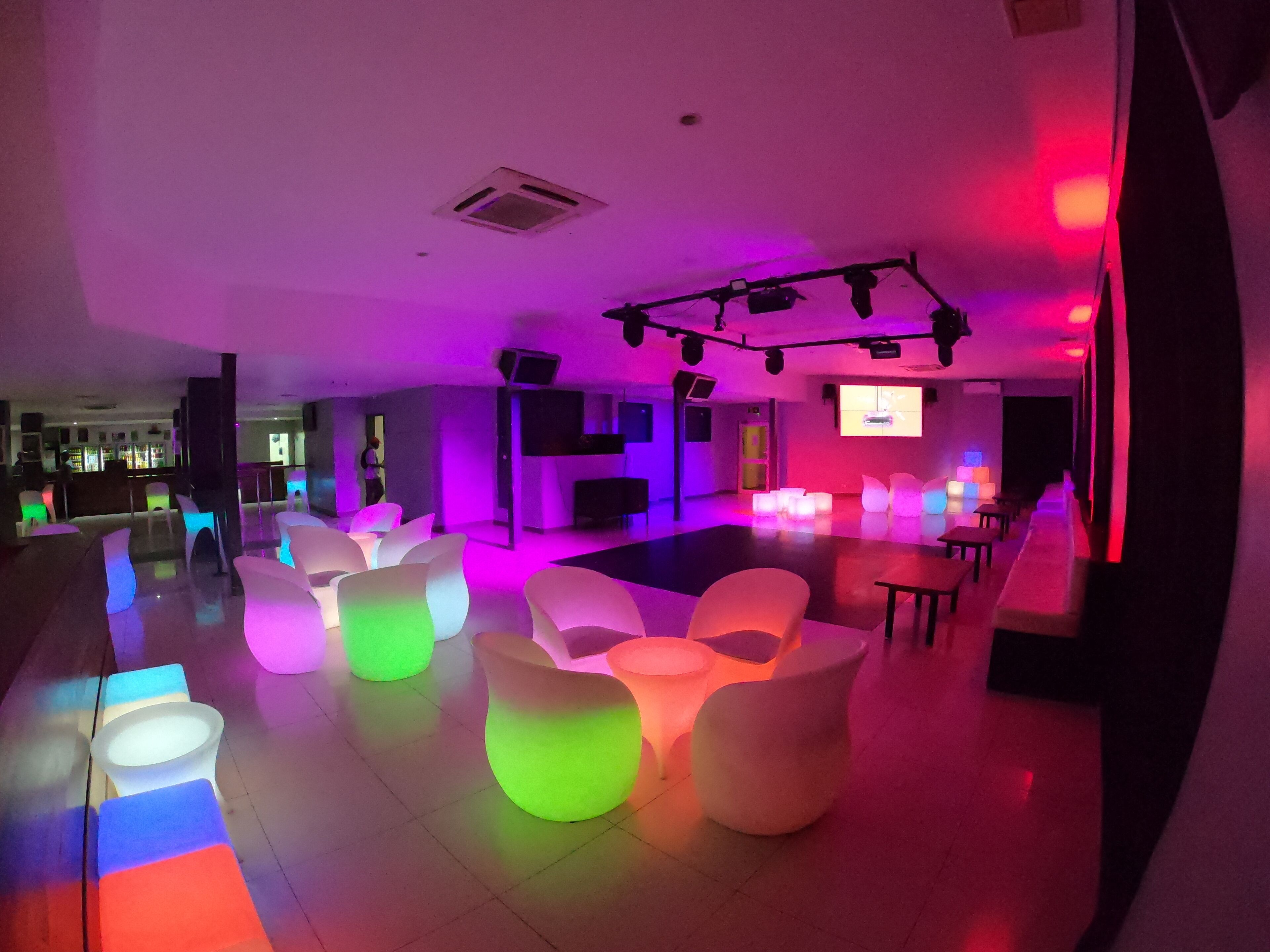 A modern lounge area with white, glowing seating and a bar in the background.