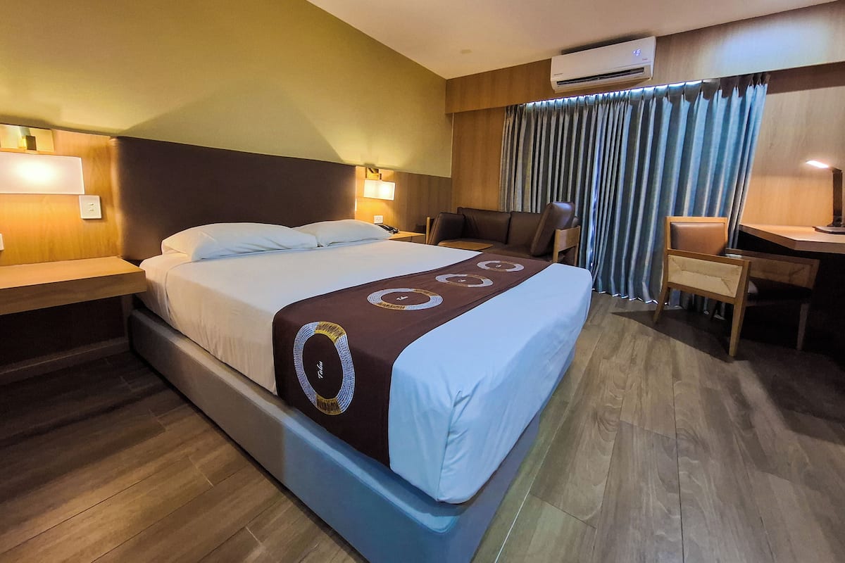 Een hotelkamer met een bed, een bureau, een stoel en een airconditioning.