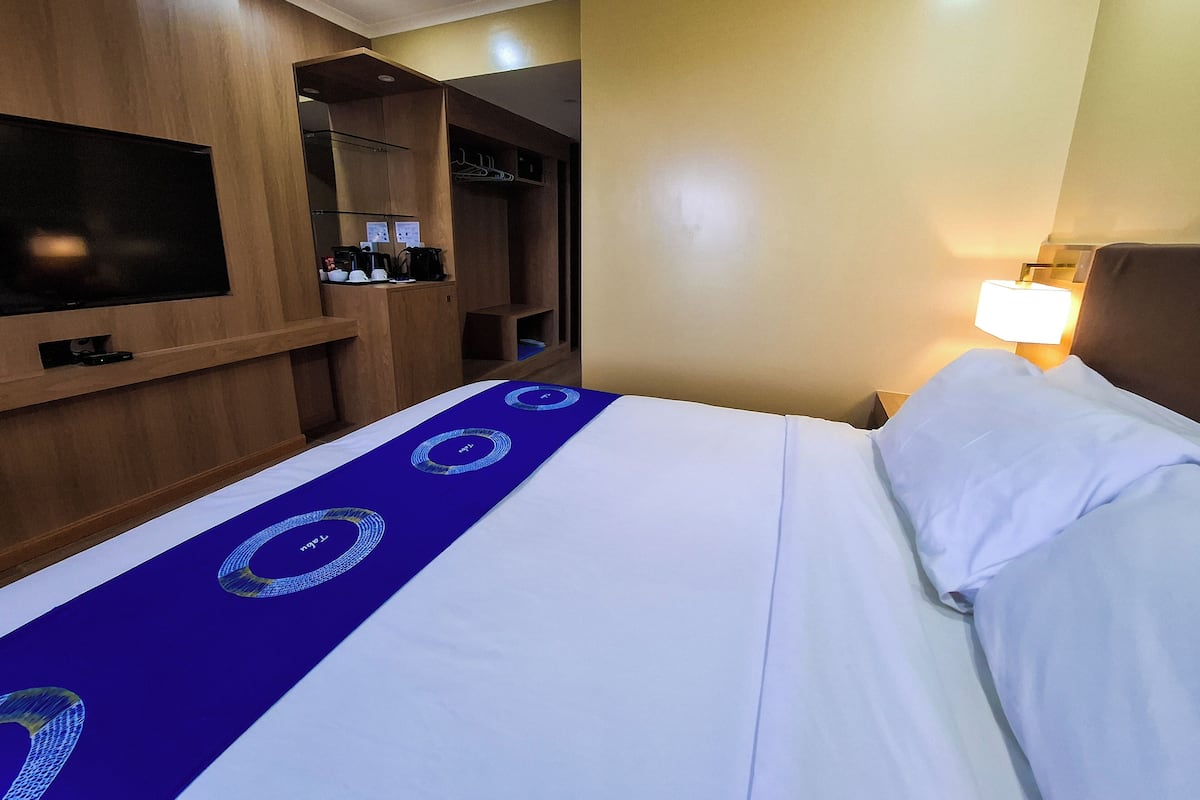 Een hotelkamer met een bed, een aan de muur bevestigde televisie, een kledingkast en een bedlampje.