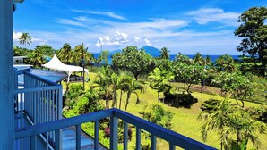 A balcony with a view of a tropical garden, a white tent, and a mountain in the distance.