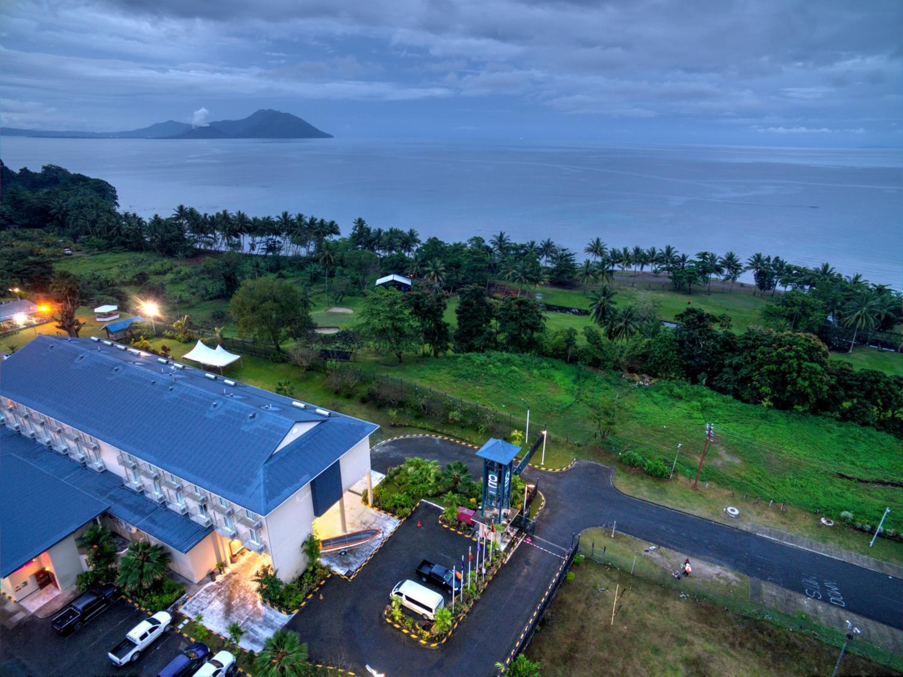A hotel with a parking area, a swimming pool, and a view of the sea and a distant island.