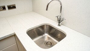 A kitchen with a stainless steel sink, a single faucet, and a countertop. - Beaconsfield Apartments (London)