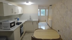A compact kitchen with a microwave, sink, and cabinets. A small dining table is in the center. - Beaconsfield Apartments (London)