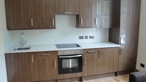A kitchen with wooden cabinets, a stainless steel sink, and a built-in oven. - Beaconsfield Apartments (London)