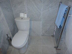 Une salle de bain avec des toilettes, un porte-serviettes avec une serviette, et deux rouleaux de papier toilette accrochés au mur.