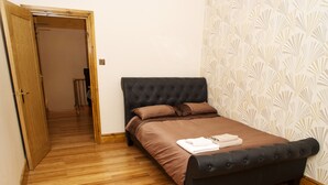 A bedroom with a bed, wooden flooring, and a patterned wallpaper. - Beaconsfield Apartments (London)