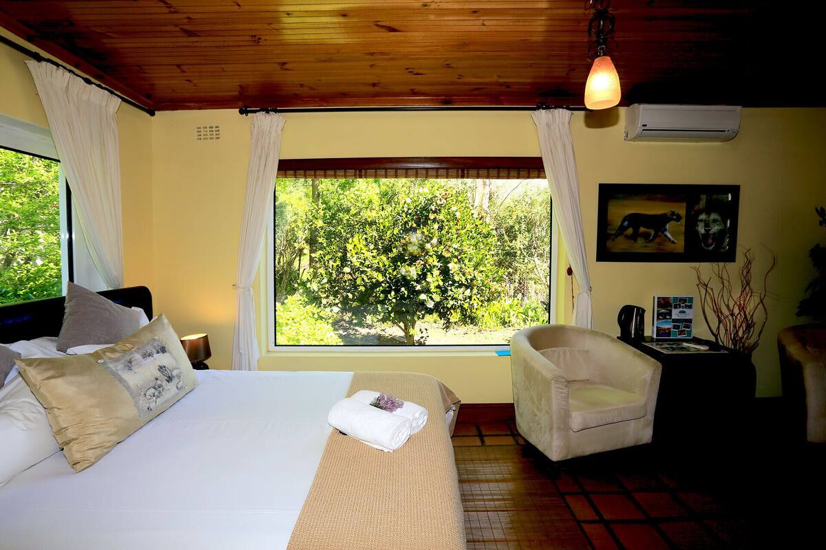 Une chambre avec un lit, une chaise, une fenêtre donnant sur des arbres et un appareil de climatisation.