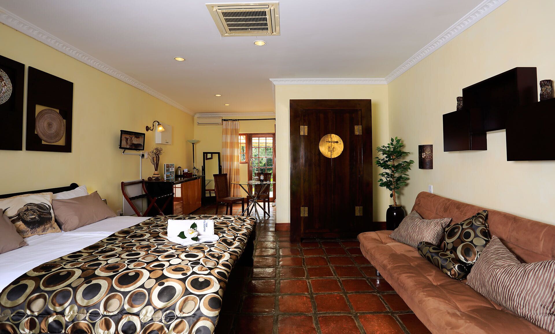 A hotel room with a bed, a sofa, a dining area, and a bathroom.