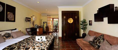 A hotel room with a bed, a sofa, a dining area, and a bathroom.