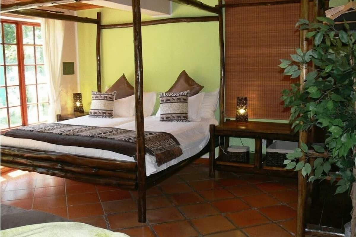 Un lit à baldaquin avec une structure en bois, deux oreillers à motifs animaliers, une table de chevet avec une lampe, et une vue sur une fenêtre avec des rideaux.