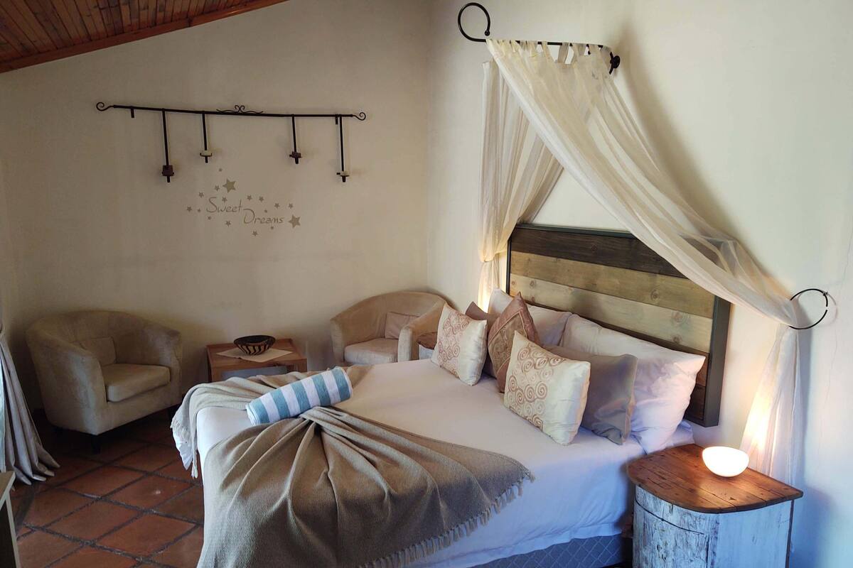 Une chambre à coucher avec un lit, deux chaises, une table de chevet et une armoire en bois.