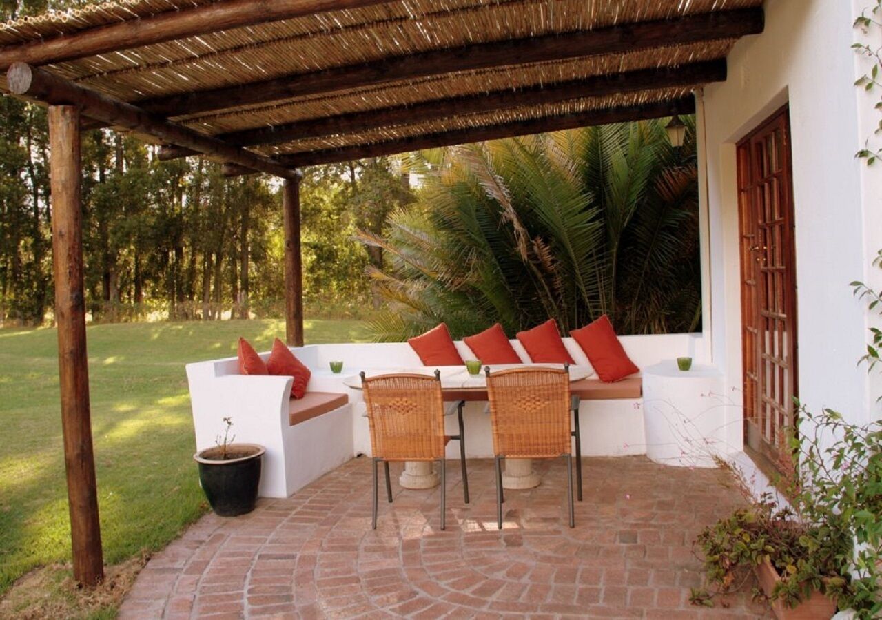 An outdoor patio with a table and chairs, a white bench with red cushions, and a potted plant.