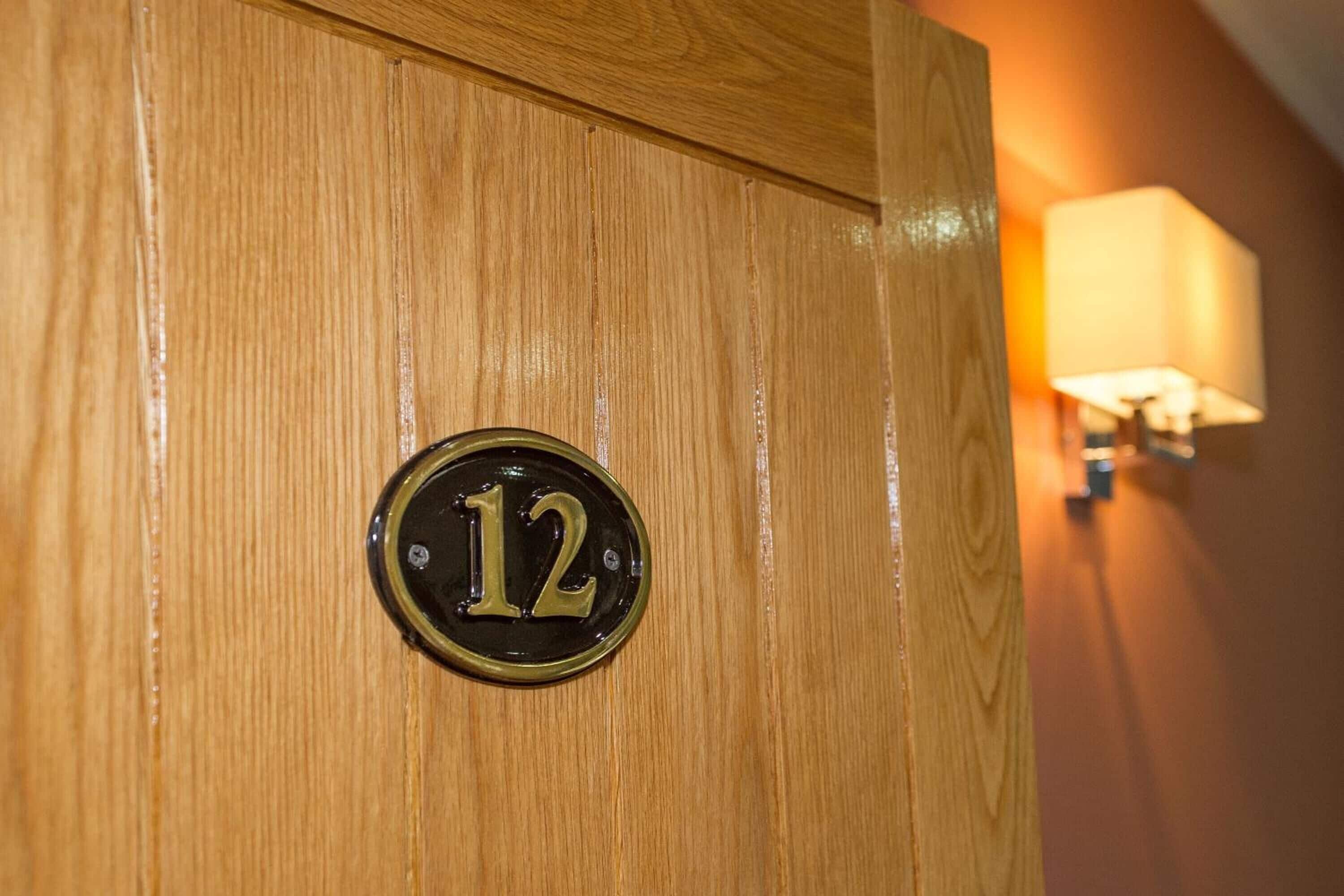 A wooden door with a brass number plate displaying the number 12.