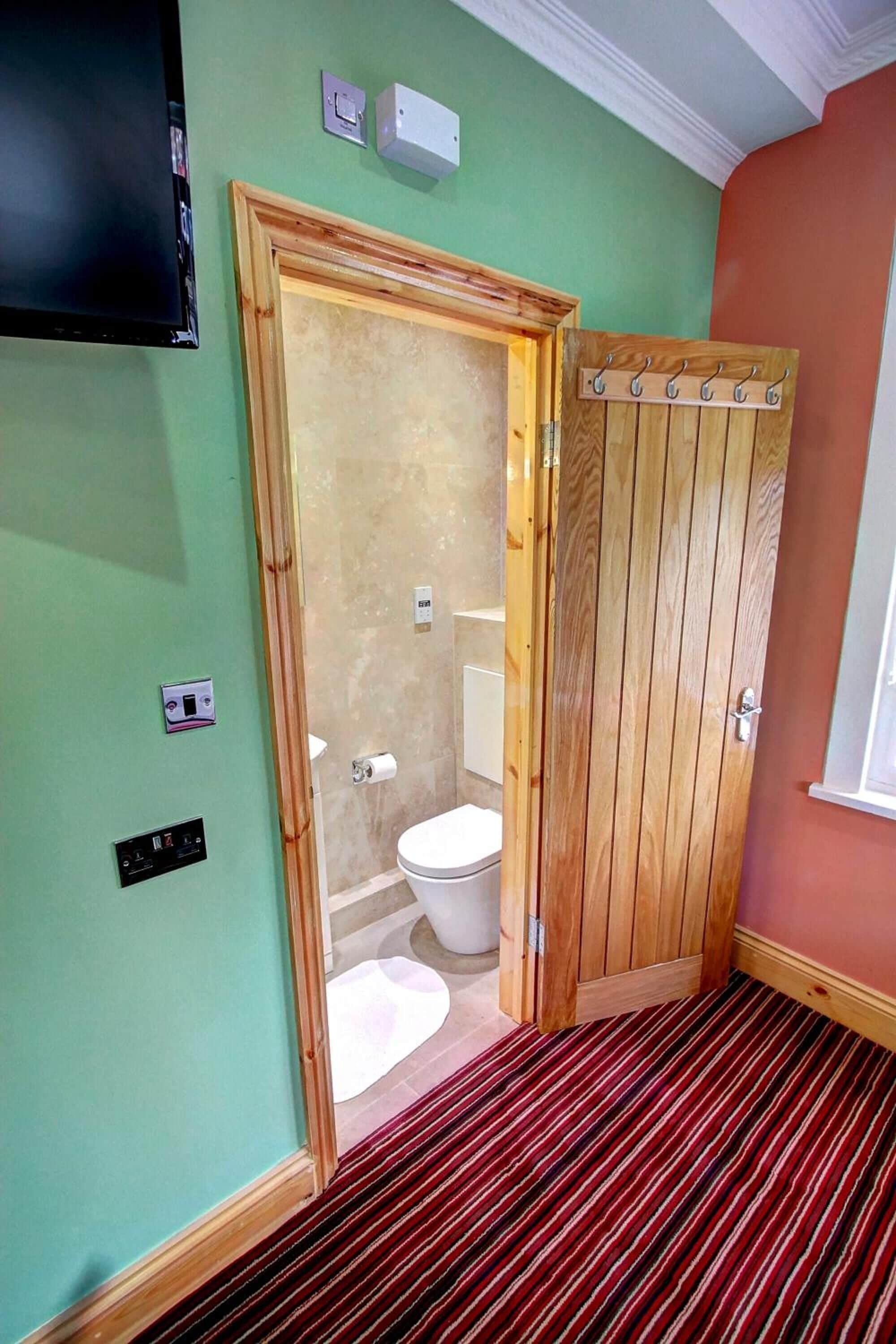 A bathroom with a wooden door, a toilet, and a shower area.