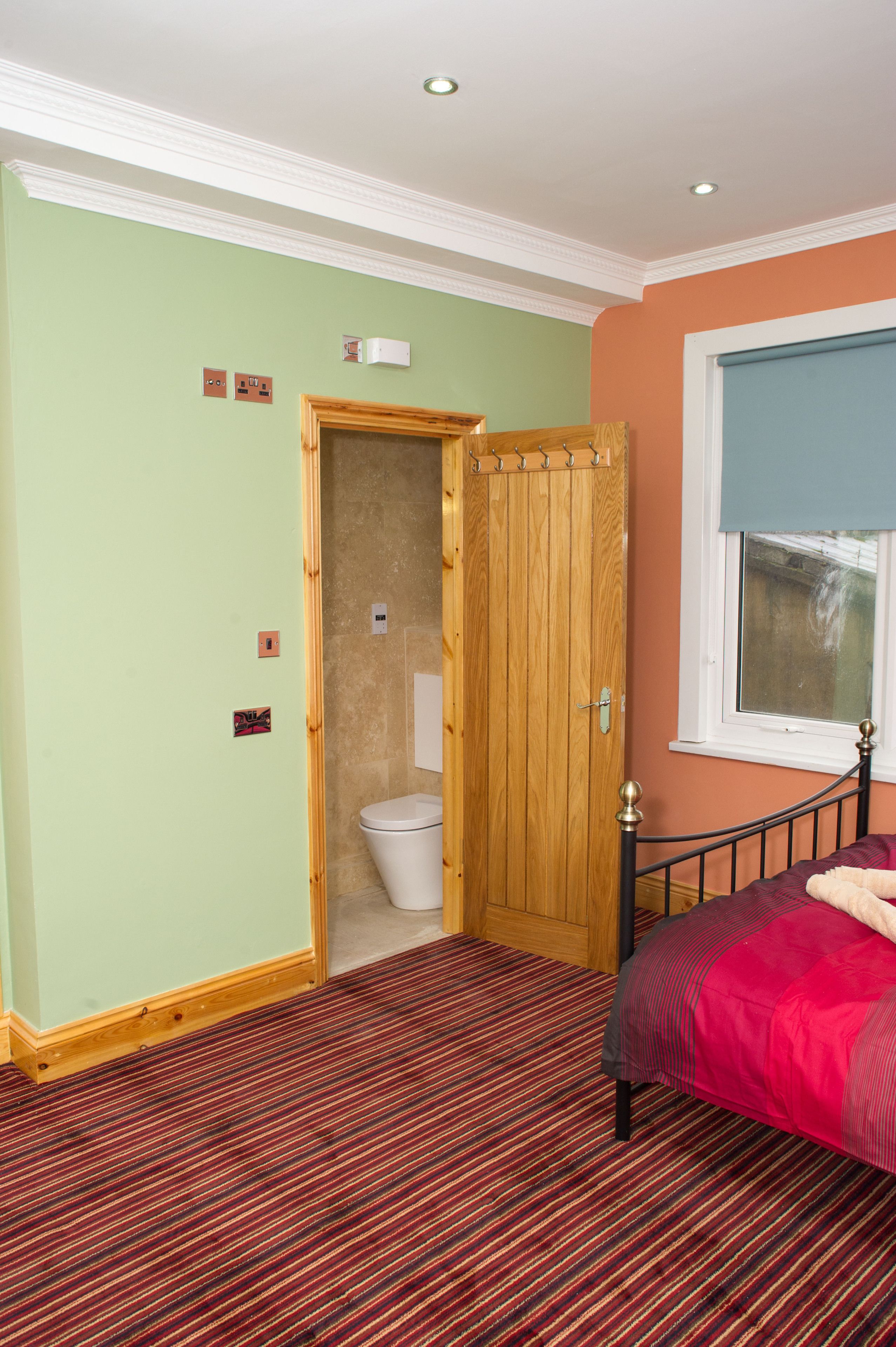 A bedroom with a bed, a wooden door, a window, and a red carpet.