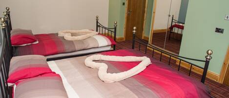 A double bed with a red and beige bedspread, a white pillow, and a white towel arranged on the bed.