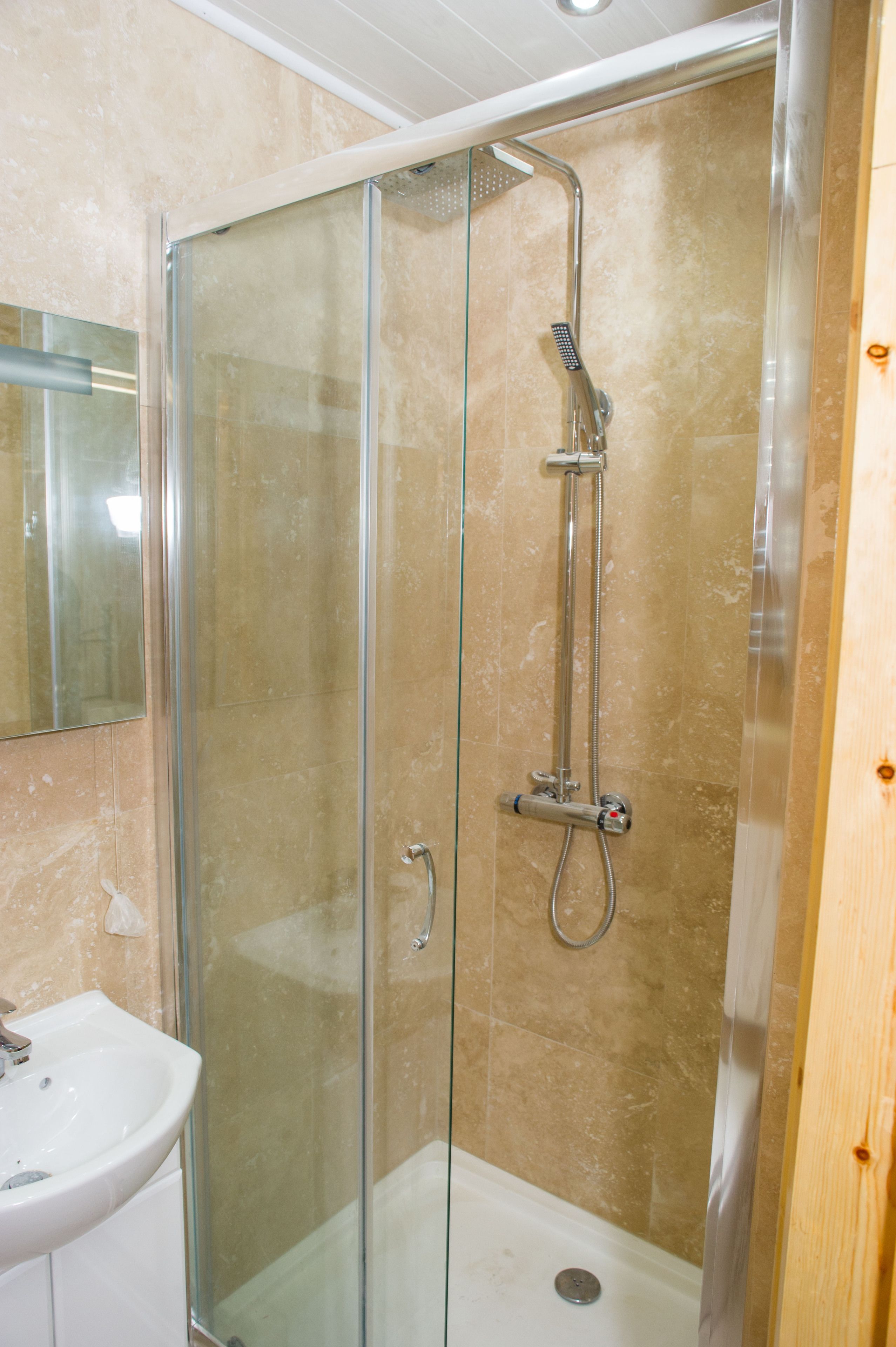 A glass-enclosed shower with a handheld showerhead and a wall-mounted faucet.
