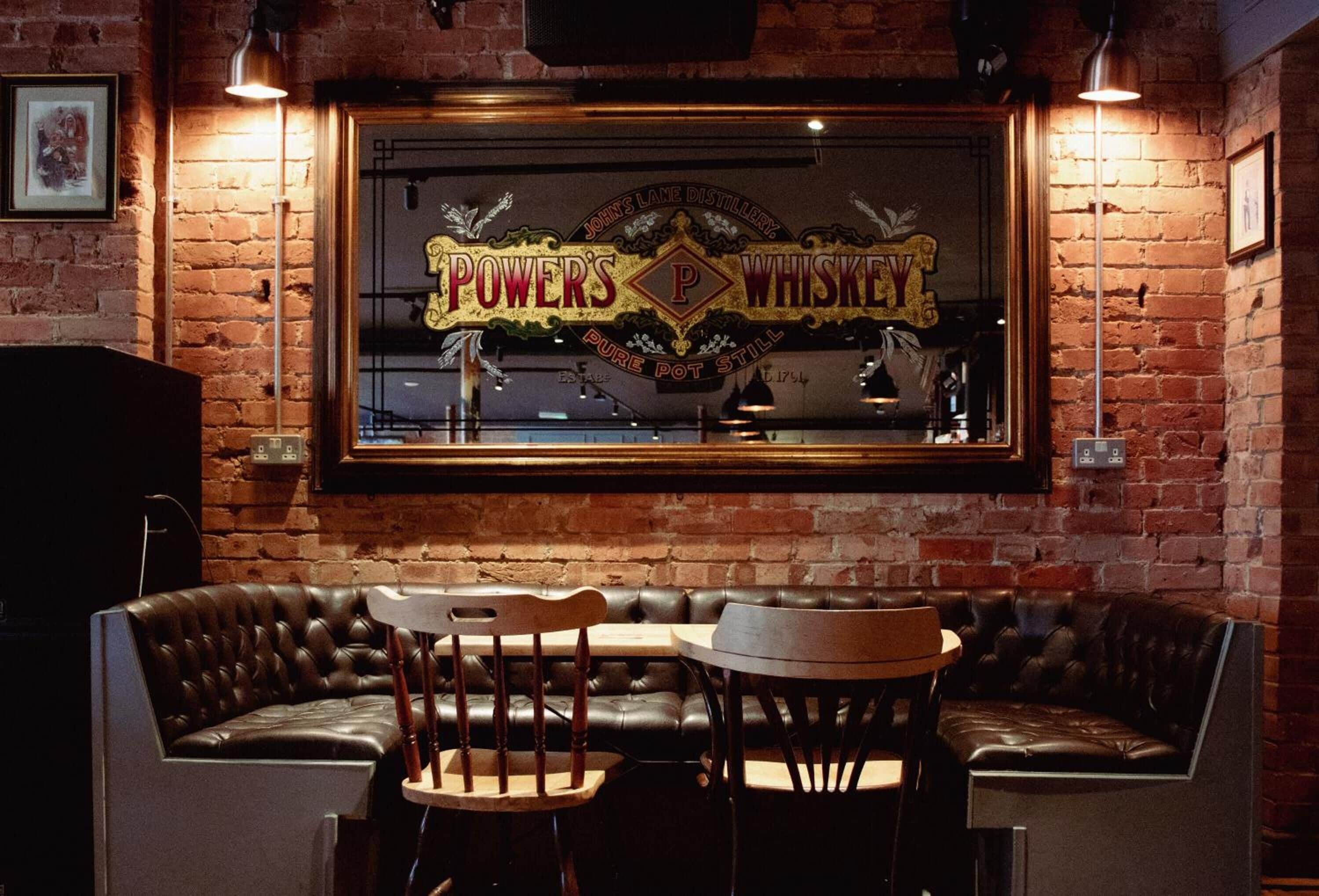 Un espace bar aux murs de briques, doté de sièges en cuir et d’une enseigne indiquant : « POWER’S WHISKEY ».