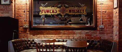 Un espace bar aux murs de briques, doté de sièges en cuir et d’une enseigne indiquant : « POWER’S WHISKEY ».
