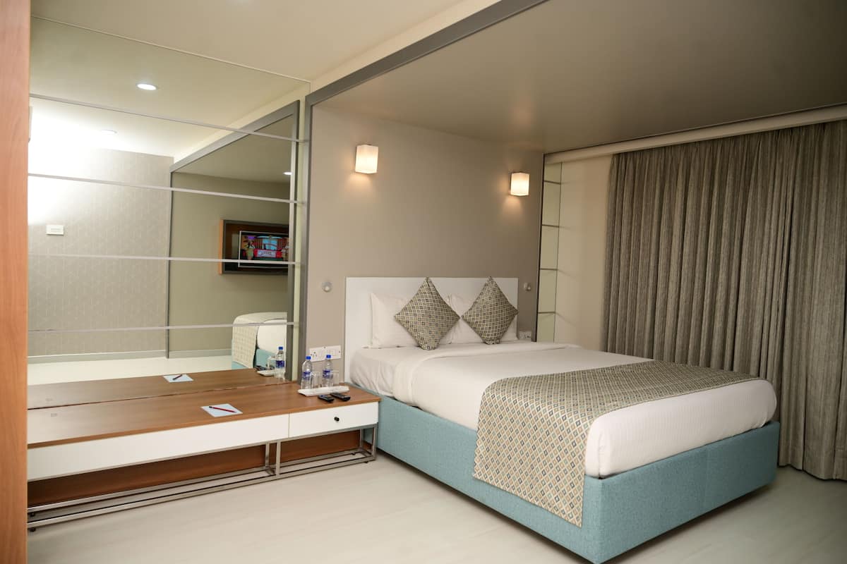 A hotel room with a bed, bedside table, mirror, and curtains.
