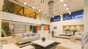 Un hall d’entrée spacieux avec un plafond haut, des luminaires modernes et un espace de détente central agrémenté de canapés et d’une table basse.