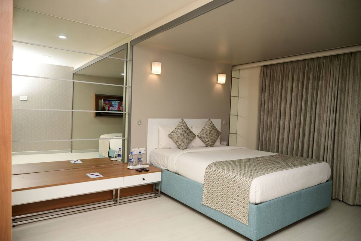 A hotel room with a bed, bedside table, mirror, and a view of the cityscape.