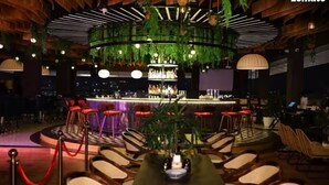 Un espace bar avec des sièges disposés en cercle, un comptoir et des plantes suspendues.