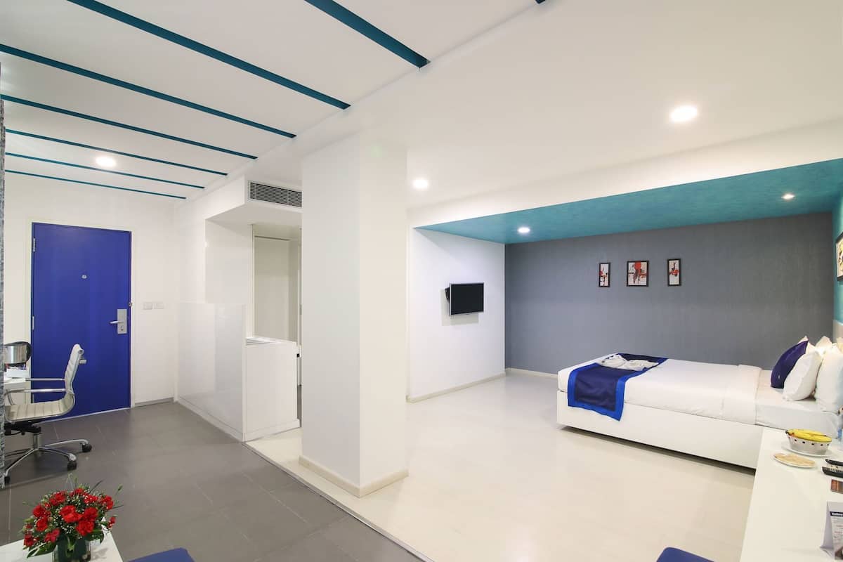 A modern hotel room with a bed, a desk, a chair, and a TV.
