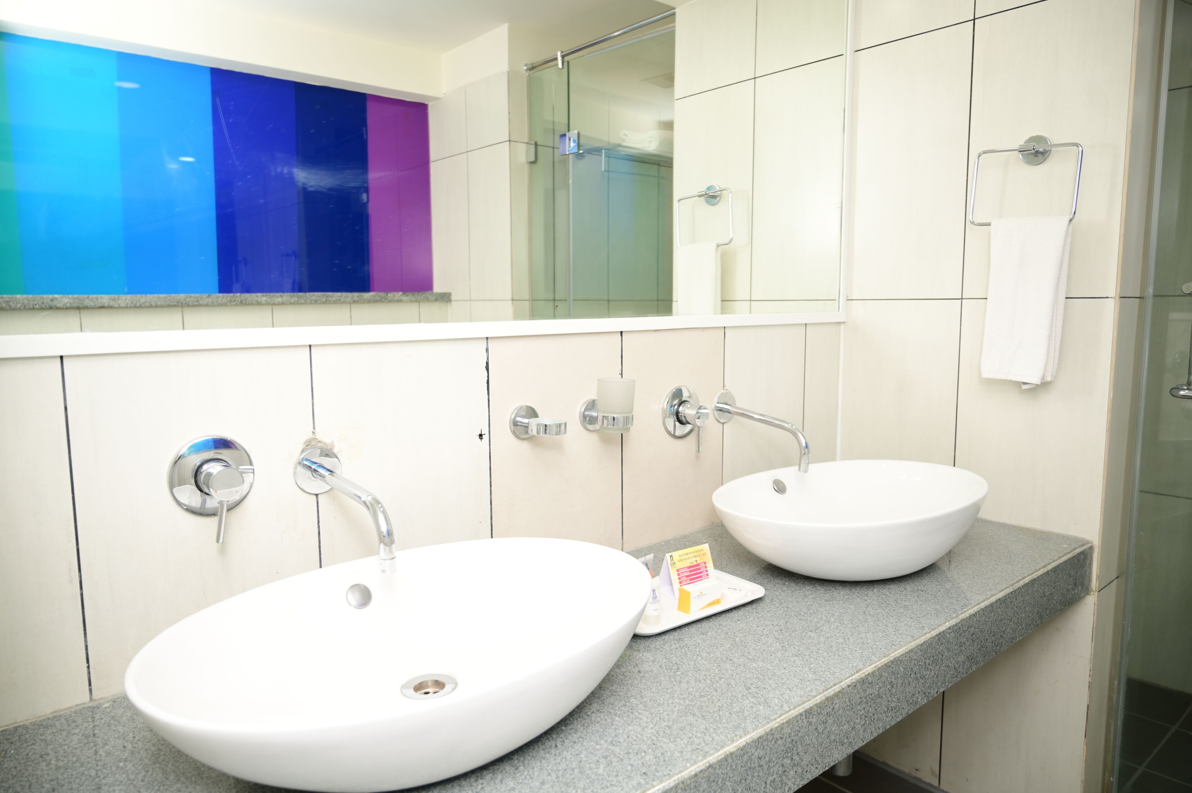 Een badkamer met twee witte wasbakken, een spiegel en een douchecabine van glas.