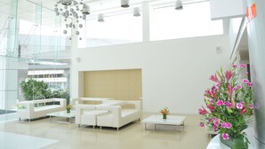 Un hall d’hôtel moderne avec un mur de verre, des canapés blancs, une table basse et un vase de fleurs.
