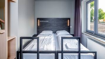 Una habitación de hotel moderna con un ventanal grande, una cama con ropa blanca y un cabecero de madera.