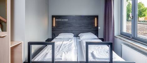 Una habitación de hotel moderna con un ventanal grande, una cama con ropa blanca y un cabecero de madera.