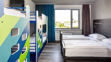 Habitación de hotel con literas, un ventanal con vistas y una cama con ropa blanca.