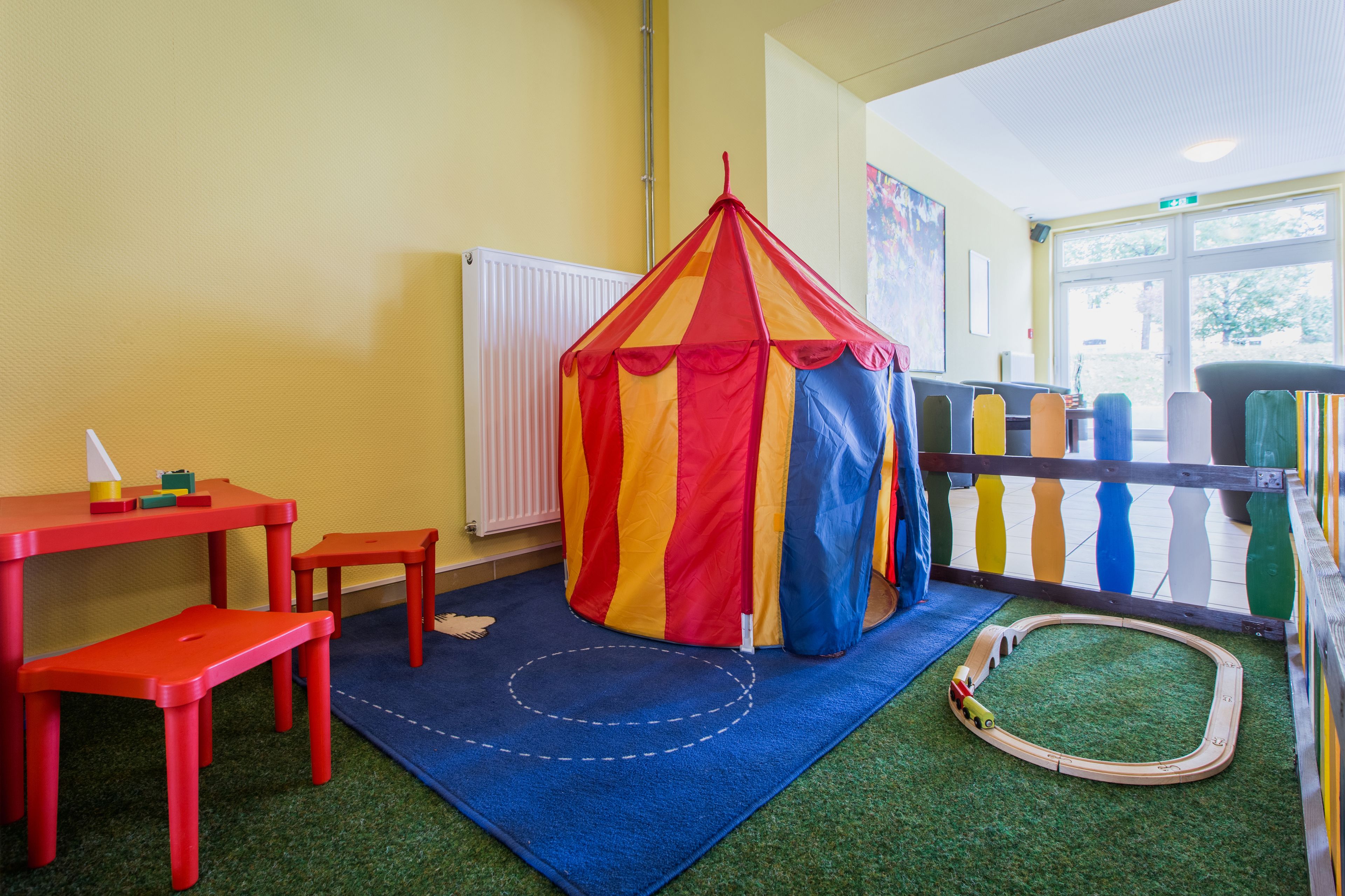 Un área de juegos con una carpa colorida, una mesita y una vía de tren de juguete.