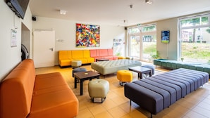 A modern lobby with orange and yellow seating, a large abstract painting, and a view of the outdoors.
