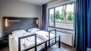 A modern hotel room with a large window, a bed with a headboard, and a wall-mounted light fixture.
