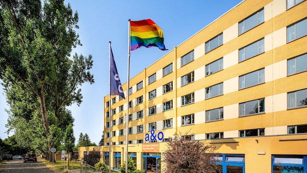 A multi-story building with a yellow facade, a rainbow flag, and a blue awning.